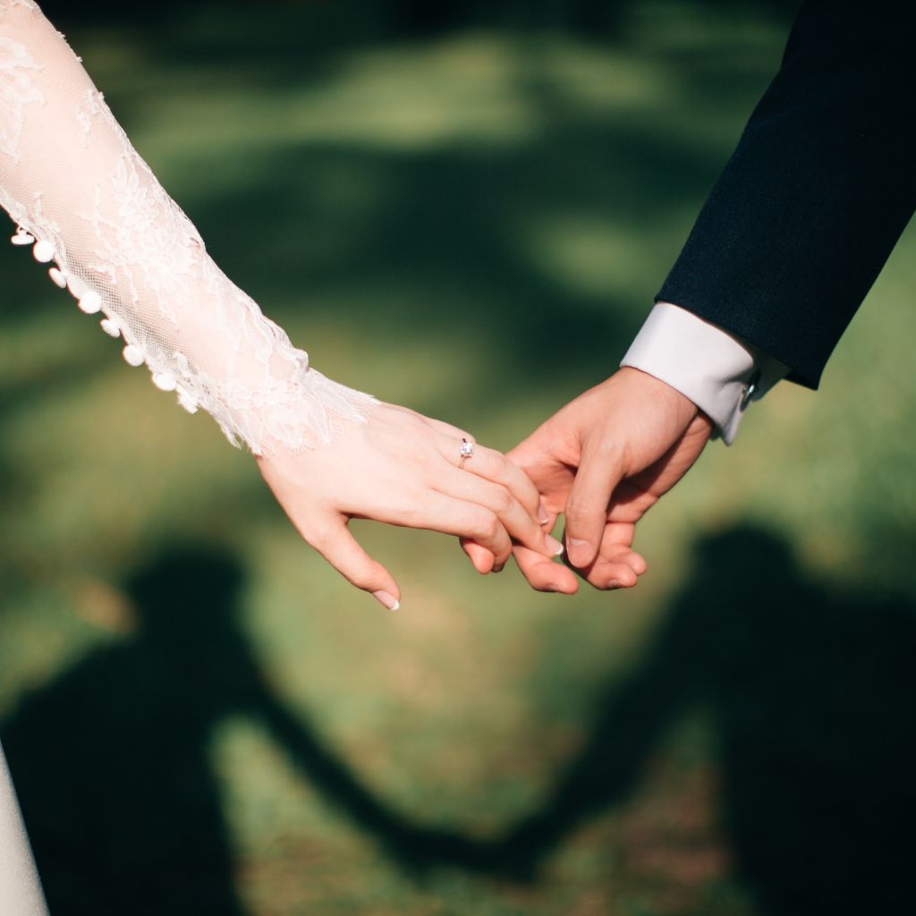 Couple holding each other's pinky fingers, suggesting a wedding or engagement moment in a garden setting