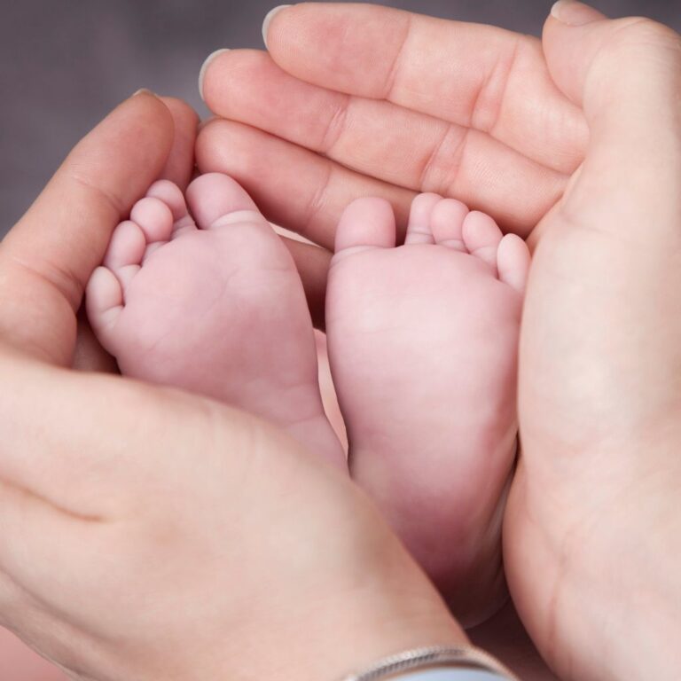 Tiny baby feet cradled in adult hands, symbolizing care and support in postpartum therapy.
