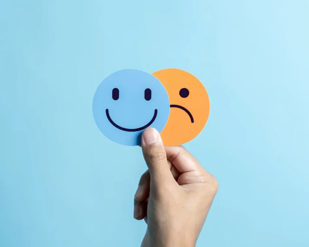 Hand holding happy and sad face icons, representing emotional states explored in therapy.